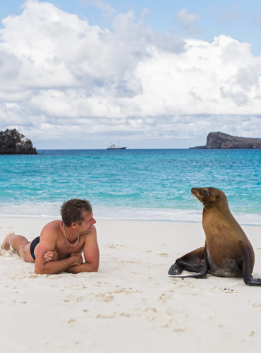 Galapagos turista acostado en la arena de galápagos mira a un lobo marino